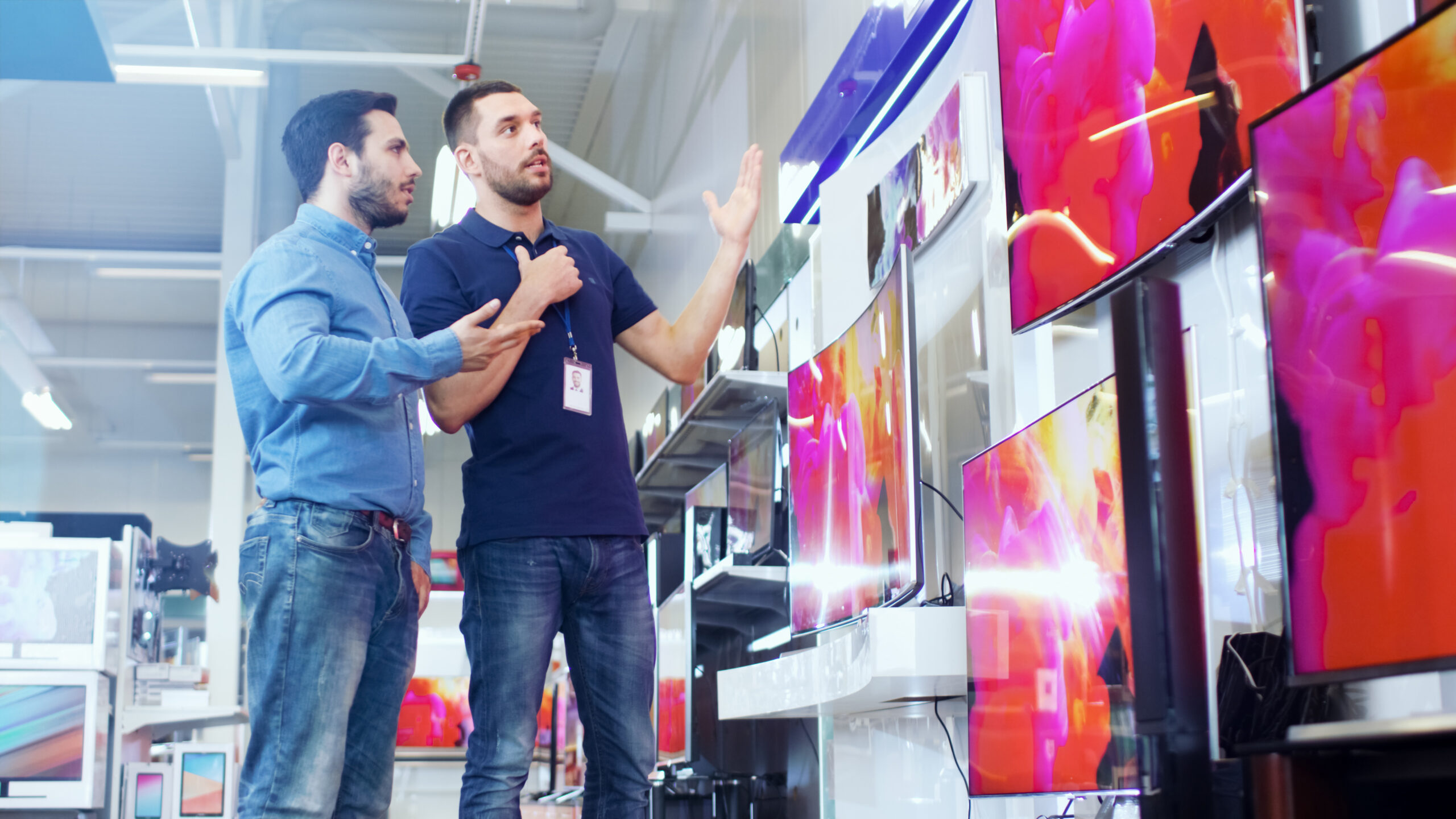 Customer and salesperson looking at a wall of TVs in a store