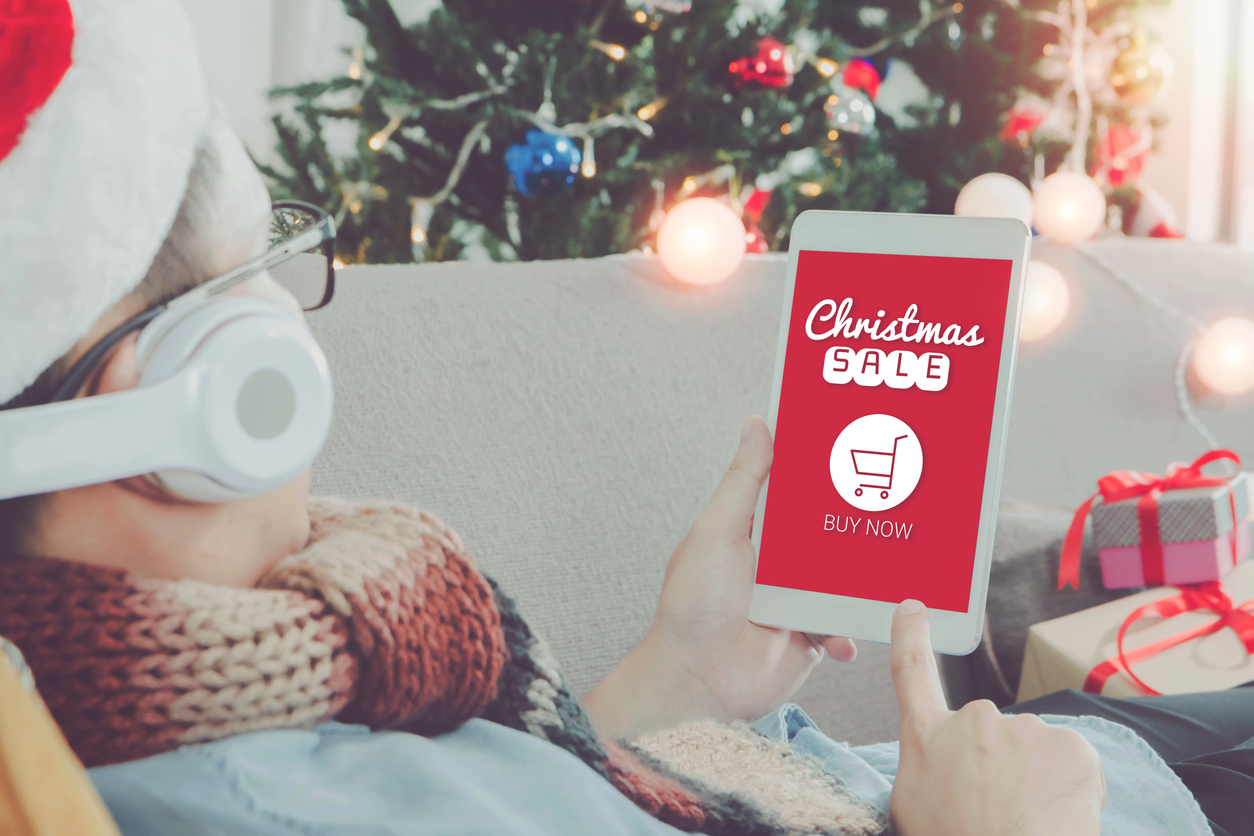 Man holding tablet with words "Christmas sale" on the screen and a Christmas tree in the background.