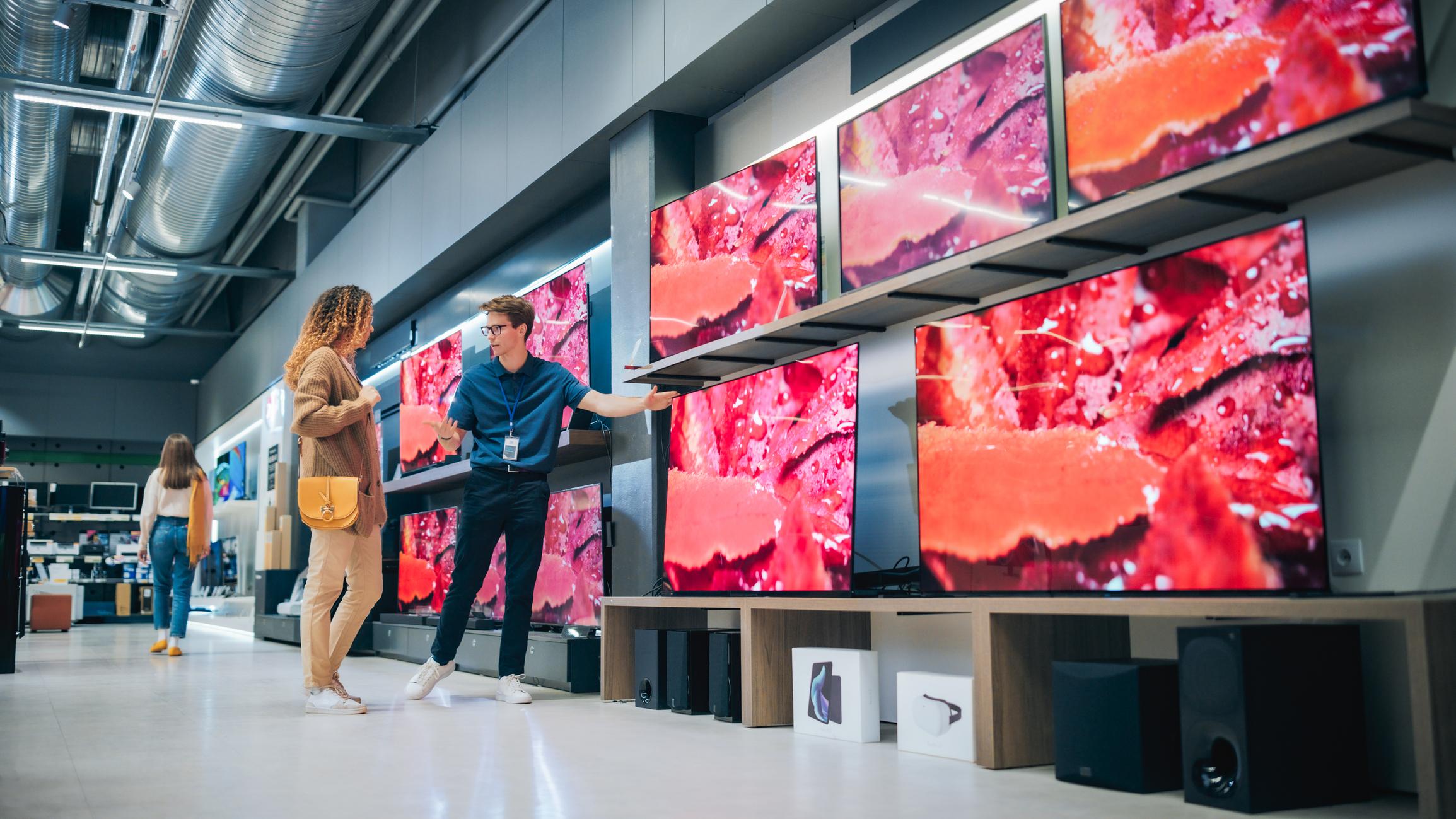 Woman and salesperson talking in an electronics store near TVs